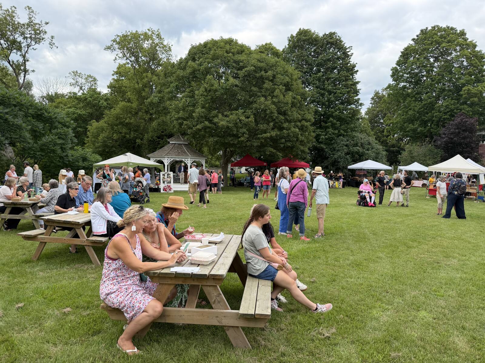 Crowd seated at picnic tables and browsing vendor tents at the market